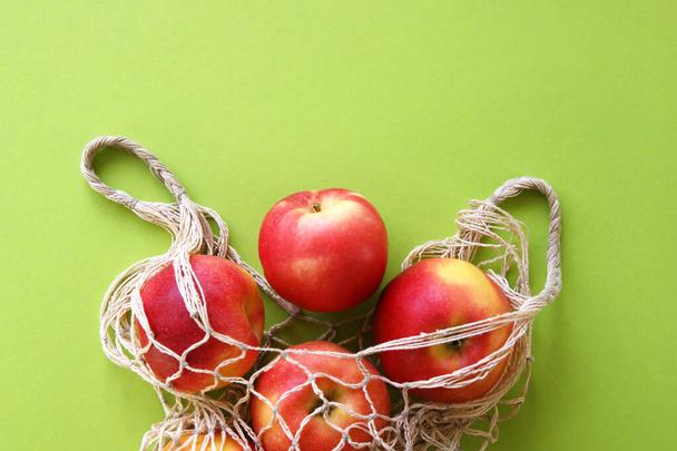 Красное яблоко и веревочный мешок на ярко-зеленом фоне. Спелые яблоки на столе и копировать пространство. Вид сверху. Лето или осень. - Фото, изображение