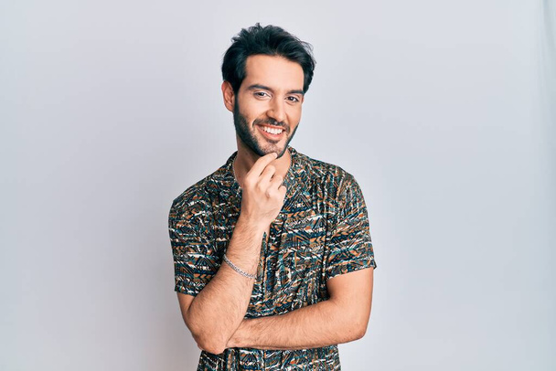 Mladý hispánec v elegantní letní košili, usmívající se sebevědomě do kamery se zkříženýma rukama a rukou na bradě. pozitivní myšlení.  - Fotografie, Obrázek