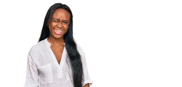 Młoda czarna kobieta w luźnych ubraniach mruga oczami patrząc w kamerę z seksowną ekspresją, radosną i szczęśliwą twarzą.  - Zdjęcie, obraz