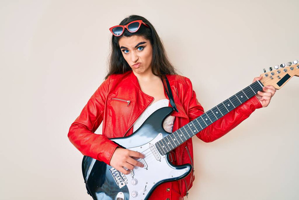 Brünettes Teenager-Mädchen spielt E-Gitarre skeptisch und nervös und runzelt die Stirn wegen des Problems. Negative Person.  - Foto, Bild