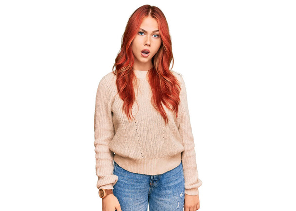 Молодая рыжая женщина в случайном зимнем свитере с шоковым лицом, выглядит скептически и саркастично, удивлена с открытым ртом  - Фото, изображение