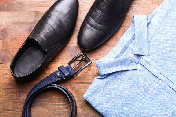 Κλασικό μπλε ανδρικό πουκάμισο με μαύρα δερμάτινα παπούτσια και ζώνη σε καφέ φόντο. Ανδρικά ενδύματα. - Φωτογραφία, εικόνα