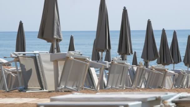 Пустой пляж на побережье морского курорта, одинокие шезлонги и закрытые серые пляжные зонтики, сорванные с пляжного курорта из-за ковида 2019 года, коронавируса, карантина, Адриатического моря, Черногории - Кадры, видео