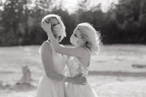 Boda de pareja lesbiana en arena blanca, use máscaras para prevenir epidemia COVID-19 - Foto, imagen