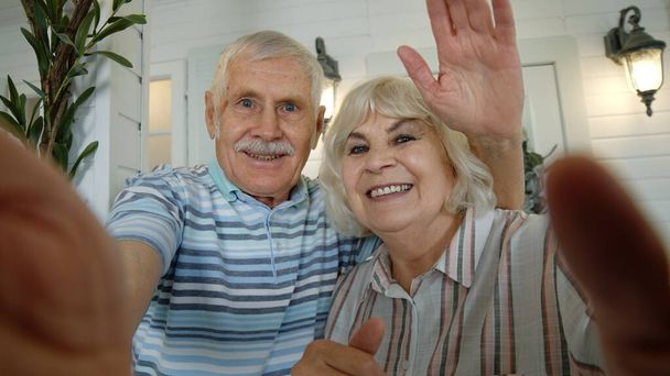 Uomo anziano, donna che fa selfie videochiamata, abbracciando, ridendo, agitando le mani, in veranda a casa - Foto, immagini