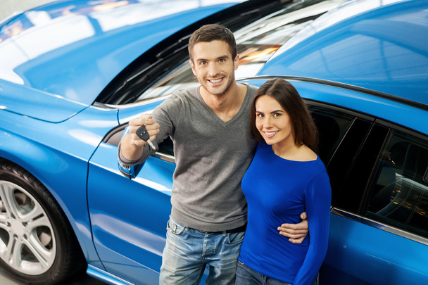 Couple standing near the car at the dealership and holding a key - Fotoğraf, Görsel