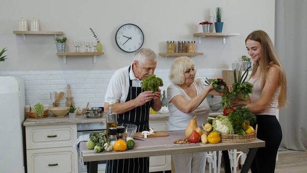Ηλικιωμένο ζευγάρι στην κουζίνα που λαμβάνει λαχανικά από το εγγόνι. Ωμά τρόφιμα υγιεινή διατροφή - Φωτογραφία, εικόνα