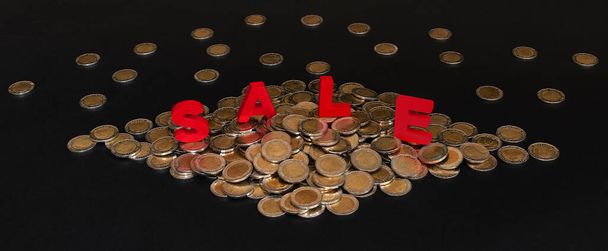 Red inscription Sale, many gold and silver coins on black background. Black Friday, seasonal holiday sales, discounts, promotions, shopping concept. Banner - Foto, afbeelding