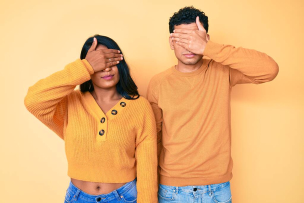 Beautiful latin young couple wearing casual clothes together covering eyes with hand, looking serious and sad. sightless, hiding and rejection concept  - Foto, Imagem