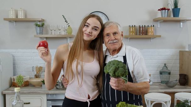 Senior grandfather with granddaughter recommending eating raw vegetable food. Vegetable diet - Photo, Image