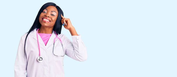 Genç Afrikalı Amerikalı kadın doktor steteskobu takıp gülümsüyor. Tek parmağıyla işaret ediyor. Harika bir fikir ya da düşünce.  - Fotoğraf, Görsel