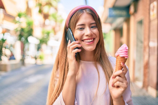 Young caucasian girl talking on the smartphone and eating ice cream at the city. - Foto, imagen