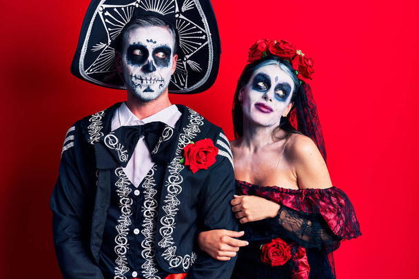 Młoda para w meksykańskim dniu martwego kostiumu z czerwonym uśmiechem patrząca w bok i patrząca myśląc.  - Zdjęcie, obraz