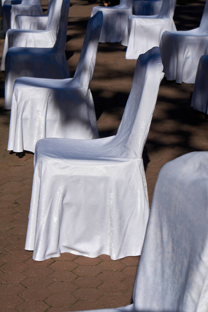 Velká skupina prázdných bílých židlí uspořádaných pro společenskou vzdálenost, připravena k posezení na venkovní obchodní konferenci. COVID-19 zdravotní a bezpečnostní opatření během pandemie vyžadují odstup mezi lidmi - Fotografie, Obrázek
