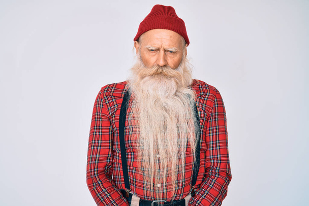 Staruszek z siwymi włosami i długą brodą w hipsterskim spojrzeniu z wełnianą czapką sceptyczny i nerwowy, marszczenie brwi zdenerwowany z powodu problemu. osoba negatywna.  - Zdjęcie, obraz