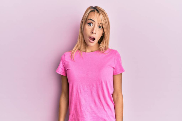 Hermosa mujer rubia vistiendo camiseta rosa casual en la cara de choque, con aspecto escéptico y sarcástico, sorprendida con la boca abierta  - Foto, Imagen