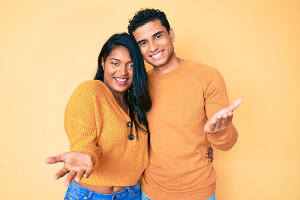 Beautiful latin young couple wearing casual clothes together smiling cheerful offering hands giving assistance and acceptance.  - Photo, Image