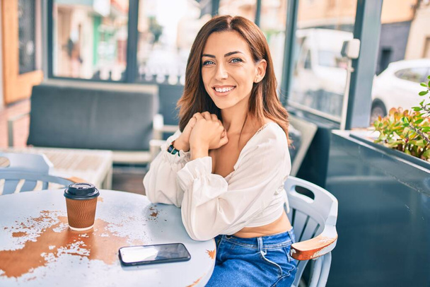Young hispanic woman smiling happy sitting at coffee shop terrace. - Foto, Imagen