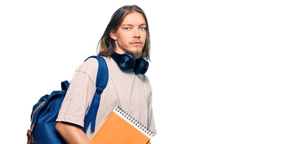 Handsome caucasian man with long hair wearing student backpack and holding books thinking attitude and sober expression looking self confident  - Foto, imagen