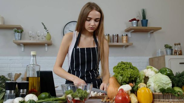 Veganerin kocht Salat mit rohem Gemüse, während sie auf digitalem Tablet nach Online-Rezept sucht - Foto, Bild
