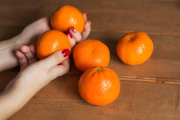 a woman's hands holding some mandarins on wood background. selective focus. - Fotografie, Obrázek