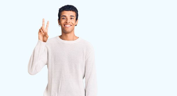 Mladý africký Američan muž na sobě ležérní oblečení ukazuje a ukazuje s prsty číslo dvě a zároveň se usmívá sebevědomě a šťastně.  - Fotografie, Obrázek