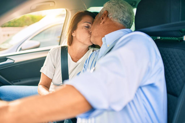 Couple d'âge moyen amoureux assis à l'intérieur de la voiture allant pour un voyage embrasser heureux et joyeux ensemble - Photo, image