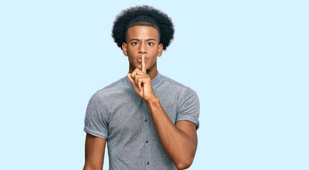 Afrikkalainen amerikkalainen mies afro hiukset yllään rento vaatteita pyytää olla hiljaa sormi huulilla. hiljaisuus ja salainen käsite.  - Valokuva, kuva