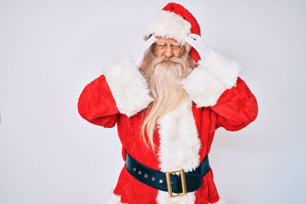 Γέρος ηλικιωμένος άνδρας με γκρίζα μαλλιά και μακριά γενειάδα φορώντας κοστούμι Santa Claus που πάσχουν από πονοκέφαλο απελπισμένος και τόνισε επειδή ο πόνος και η ημικρανία. χέρια στο κεφάλι.  - Φωτογραφία, εικόνα