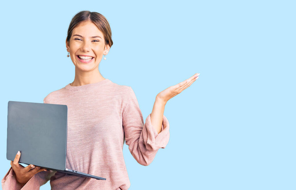 Piękna biała kobieta z blond włosami pracuje przy użyciu laptopa świętując zwycięstwo szczęśliwym uśmiechem i ekspresją zwycięzcy z podniesionymi rękami  - Zdjęcie, obraz