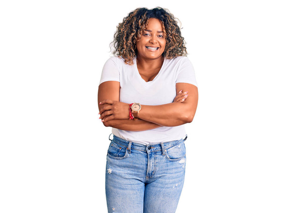 Jeune femme afro-américaine plus taille portant des vêtements décontractés visage heureux souriant avec les bras croisés regardant la caméra. personne positive.  - Photo, image