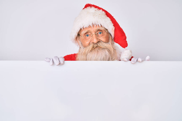 Старик с седыми волосами и длинной бородой в костюме Санта Клауса с плакатом, улыбающимся счастливой и прохладной улыбкой на лице. показывая зубы.  - Фото, изображение