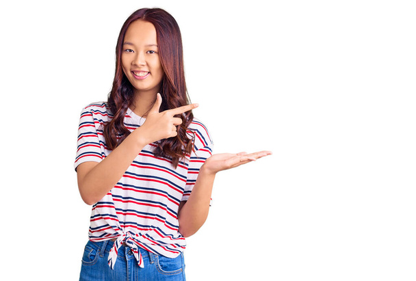Mladý krásný číňan dívka na sobě ležérní oblečení ohromen a usmívá se na kameru při prezentaci s rukou a ukazuje prstem.  - Fotografie, Obrázek