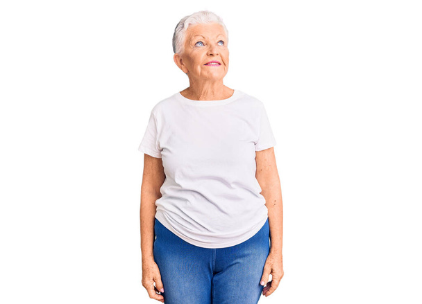 Senior gyönyörű nő kék szemekkel és ősz haj visel alkalmi fehér póló mosolygós oldalra néz, és bámul félre gondolkodás.  - Fotó, kép