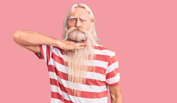 Oude oudere man met grijs haar en lange baard met gestreepte tshirt die de keel doorsnijdt als mes, dreigt agressie met woedend geweld  - Foto, afbeelding