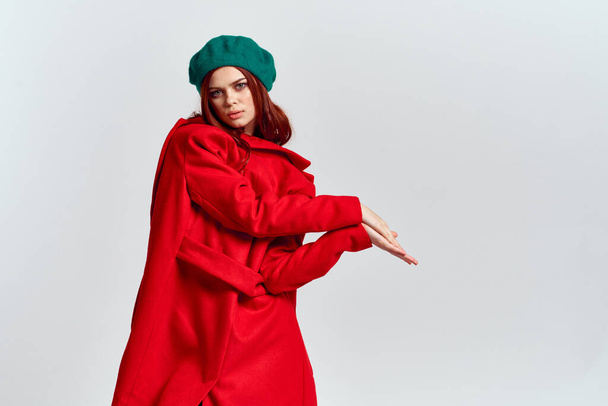 A woman holds in her hand a red coat and a dark T-shirt Green hat cropped view of a light background - Photo, Image