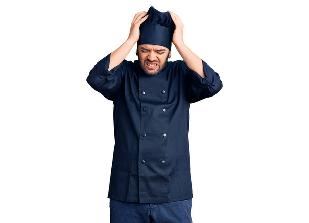 Young hispanic man wearing cooker uniform suffering from headache desperate and stressed because pain and migraine. hands on head.  - Photo, Image