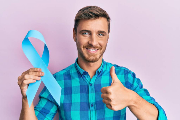 Красивый белый мужчина с голубой лентой, улыбающийся счастливый и позитивный, большой палец вверх, отлично справляющийся и одобряющий знак  - Фото, изображение