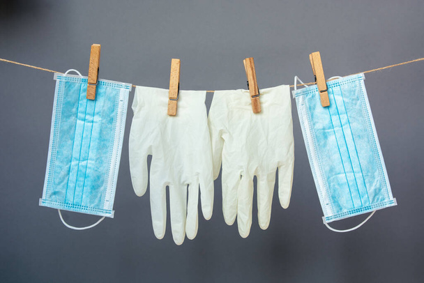 latex gloves and a medical face mask hang on clothespins on a gray background. safety concept during the coronavirus pandemic. - Foto, Imagem