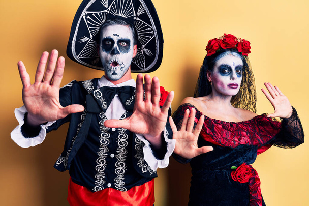 Młoda para ubrana w meksykański dzień martwego kostiumu na żółto zatrzymuje gest dłońmi, gniewną i frustrującą ekspresję  - Zdjęcie, obraz