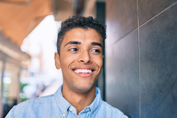 Jeune homme latino souriant heureux marchant à la ville. - Photo, image