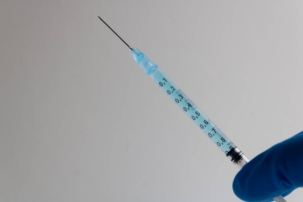syringe with needle and blue medicine held with a blue latex glove isolated on a white background - Photo, Image