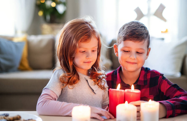 Small girl and boy indoors at home at Christmas, holding candles. - Фото, зображення