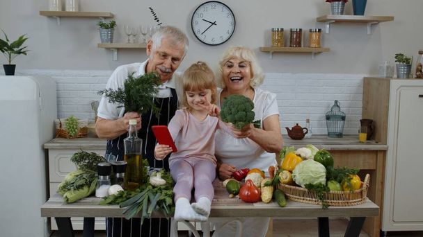 Blogcu kız, mutfakta sebzeli yaşlı çiftle telefonda selfie çekiyor. - Fotoğraf, Görsel
