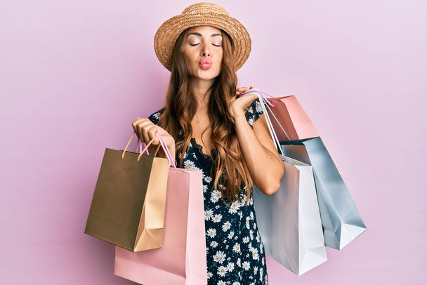 Young brunette woman holding shopping bags looking at the camera blowing a kiss being lovely and sexy. love expression.  - Fotoğraf, Görsel