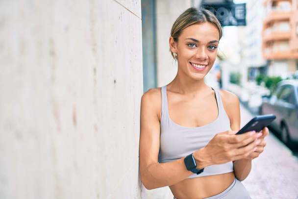 Jovem cauciasiano fitness mulher vestindo roupas esportivas de treinamento ao ar livre usando smartphone - Foto, Imagem