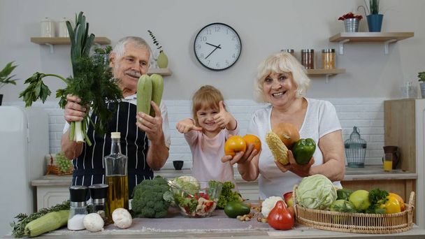 Grandchild girl with senior grandparents recommending eating raw vegetable food. Nutrition diet - Photo, Image
