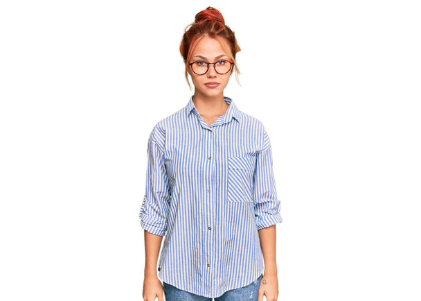 Young redhead woman wearing casual clothes and glasses with serious expression on face. simple and natural looking at the camera.  - Fotografie, Obrázek