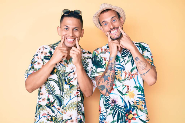 Nuoret homopari kaksi miestä yllään kesähattu ja Havaijin paita hymyilee suu auki, sormet osoittaa ja pakottaa iloinen hymy  - Valokuva, kuva