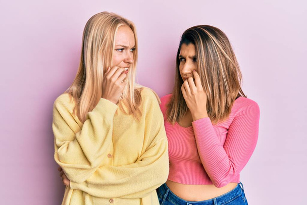 Kaksi ystävää seisoo yhdessä vaaleanpunainen tausta näyttää stressaantunut ja hermostunut kädet suulla puree kynnet. ahdistuneisuusongelma.  - Valokuva, kuva